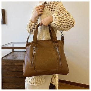 Close-up of caramel brown tote bag featuring decorative metal zippers and fine leather texture