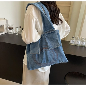 Blue denim tote bag with red stitching and external pocket on the shoulder strap