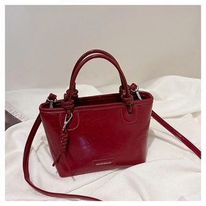 Détail du sac seau bordeaux avec poignée nouée et logo de marque sur surface texturée