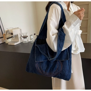 Detail of dark blue denim tote bag with orange circular embroidery and wide strap