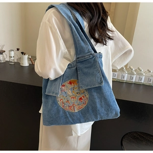 Détail du sac cabas en denim avec broderie circulaire porté à l'épaule du modèle