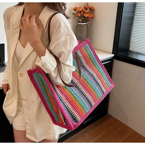 Detail of colorful rainbow striped straw tote bag with brown leather handles worn by model