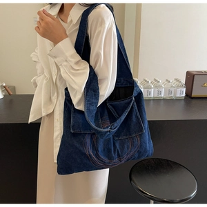 Detail of blue denim tote bag featuring orange circular embroidery and a side flap pocket
