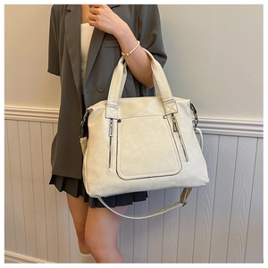Detail of cream white tote bag featuring decorative zippers and adjustable strap