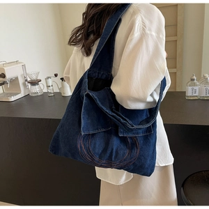 Detail of blue denim tote bag with red circular stitching shown on a person
