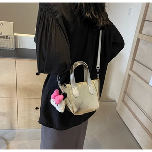 Detail of a metallic gold bucket bag with a cute plush charm and crossbody strap