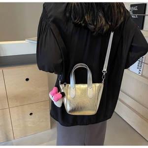 Detail of champagne gold metallic bucket bag with pink bow charm and silver handle