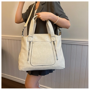 Close-up of cream leather tote bag featuring pleated texture and dual vertical zippers