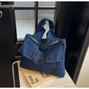 Detail of dark blue denim tote bag with vibrant orange circular embroidery and side pockets