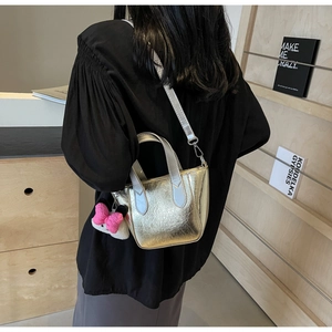 Detail of a gold metallic handbag with cracked texture, silver strap and plush bow charm