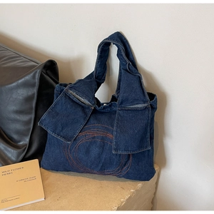 Detail of dark blue denim tote bag with orange circular embroidery and wide strap