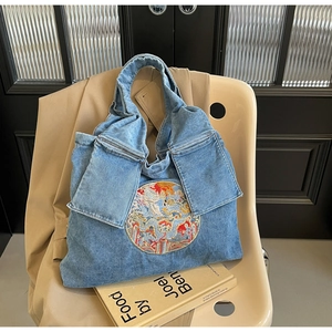 Détail d'un sac cabas en jean bleu avec broderie vintage et rabats de poches stylés
