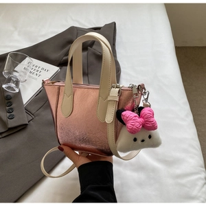 Detail of metallic pink bucket bag with cream handle and cute plush charm on white bedding