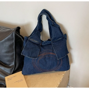 Detailed shot of dark blue denim tote bag with orange circular embroidery and sleek stone backdrop