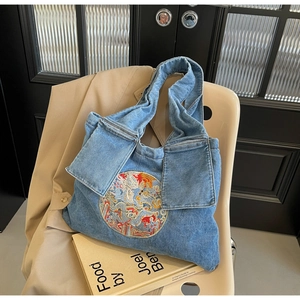 Détail de la broderie de dragon colorée sur un grand cabas en jean bleu au style ethnique