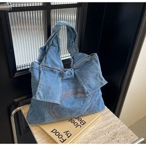 Close-up of blue denim tote bag featuring orange circular embroidery and decorative flaps