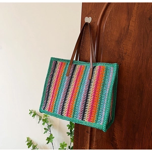 Detail of multi-color woven straw tote bag with brown leather handles hanging on a hook