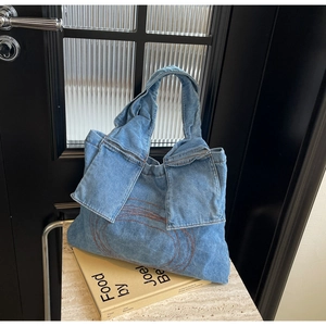 Detail shot of a denim tote bag with red embroidery on a minimalist artistic background