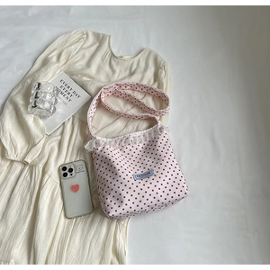 Dettaglio della borsa a secchiello in nylon a pois con pizzo su sfondo vestito bianco crema