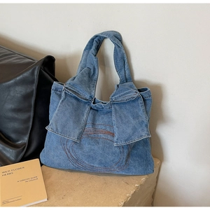 Detail of blue denim handbag featuring side bow accents and embroidered circle pattern