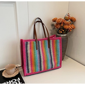 Detailed close-up of rainbow striped straw tote bag with brown leather handles and decor