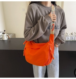 Detail of orange nylon crossbody bag featuring floral wide strap and textured side zipper