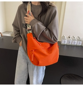 Detail of bright orange nylon crescent bag with floral jacquard strap and woven zipper pull