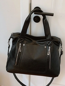 Large black faux leather tote bag with silver zippers hanging on white door handle