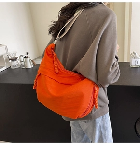 Detail showing an orange nylon crescent crossbody bag worn by a model in a cafe