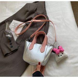 Detail of silver metallic tote bag with pink bow pendant and plush doll accessory