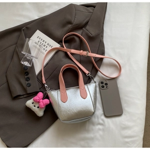 Detail of silver metallic handbag with pink handles and plush cat charm on a brown blazer