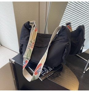 Detail of black nylon hobo bag with colorful embroidered strap and woven zipper puller