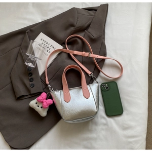 Macro detail of silver textured crossbody bag with pink handle and plush doll charm