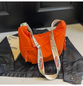 Detail of vibrant orange nylon crescent bag with patterned jacquard strap on leather jacket