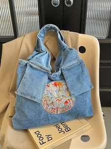 Sac cabas en jean bleu avec broderie dragon et grandes poches à rabat sur un fauteuil