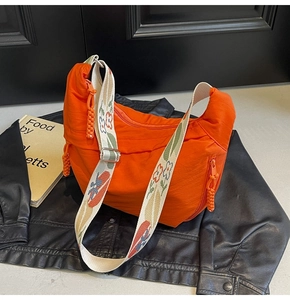 Detail of orange nylon crescent bag featuring a floral patterned wide shoulder strap