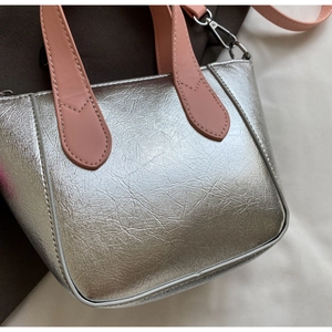 Detail of silver metallic tote bag with pink handle and textured cracked leather finish