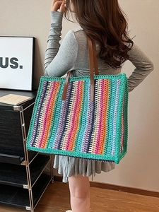 Large colorful striped straw tote bag with brown leather shoulder straps shown on model