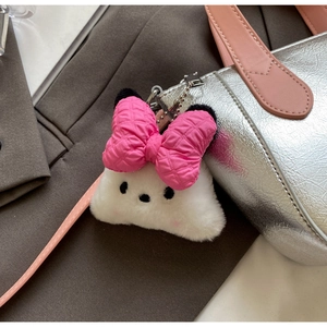Close-up of cute white plush charm with pink quilted bow on a silver textured bag