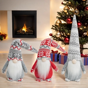 Close-up of three Christmas gnomes with snowflake knitted hats near a warm fireplace