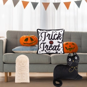 Halloween pillow set with Trick or Treat motifs and black cat plush on a cozy gray sofa