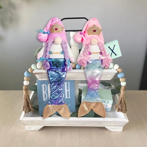 Detail of mermaid gnome dolls with metallic tails and crown decorations on a white tray