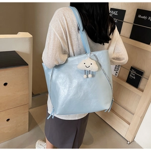 Detailed view of light blue tote bag with decorative zippers and plush cloud pendant charm