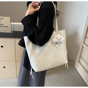 Detail of white tote bag featuring side zipper, thin strap and fluffy cloud charm