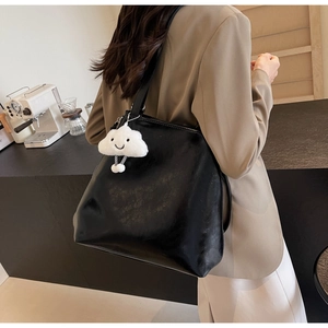 Close-up of black leather tote bag featuring a cute white plush cloud charm on the strap
