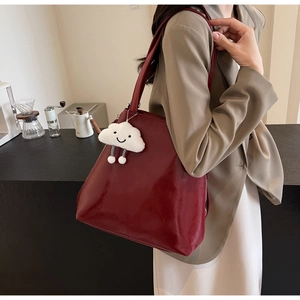 Detail of burgundy tote bag with a white plush cloud charm shown in a city setting