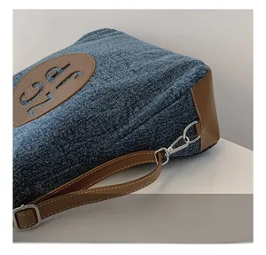 Detail of silver metal hook and brown leather trim on a blue denim shoulder bag