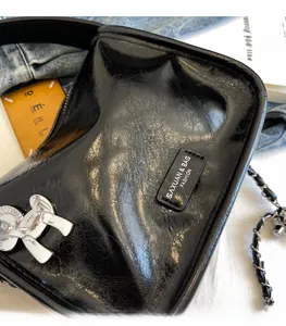 Dettaglio borsa in pelle nera stropicciata con stemma a cavallo argento e tracolla a catena