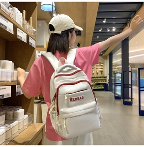 White casual backpack with red zippers and RKDBAG patch shown on a female model