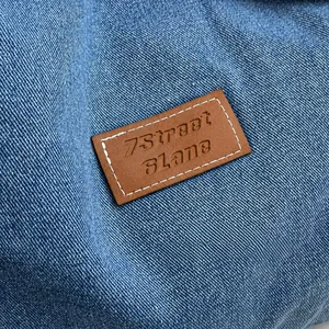 Macro della toppa in pelle marrone sullo zaino in denim blu con cuciture dettagliate